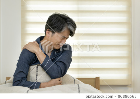 Middle-aged man sitting on the bed and holding his shoulders with his hands Middle-aged man sitting on the bed and holding his shoulders with his hands 86886563