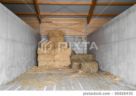 Yellow dry haystacks in square shape stand on top of each other in concrete shed 86888430