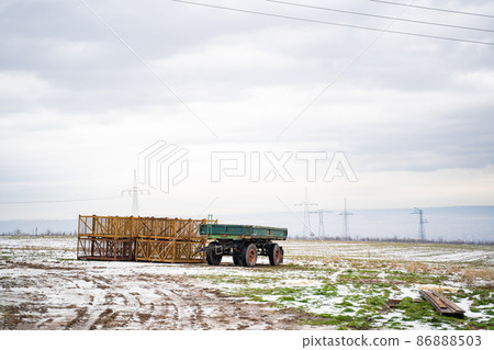Green tractor trailer on farm in field near agricultural fixtures in winter snow Green tractor trailer on farm in field near agricultural fixtures in winter snow 86888503