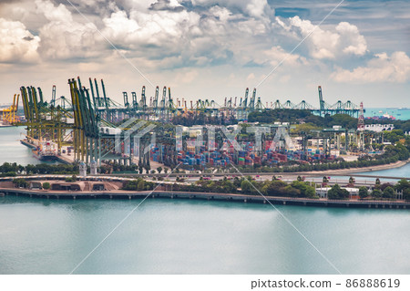 The huge busiest logistic port in Singapore, plenty of cranes to move containers, huge cargo ships in the background, skyscrapers on background 86888619