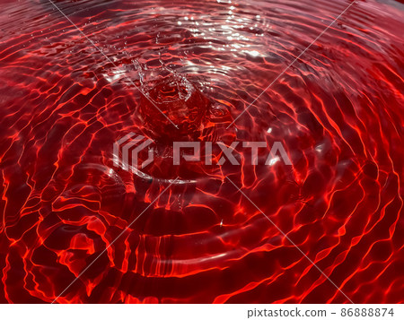 Close-up rain drips on a red background and leaves circles on the water. Close-up rain drips on a red background and leaves circles on the water. 86888874