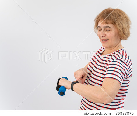Elderly woman looking at fitness bracelet while exercising on white background. 86888876