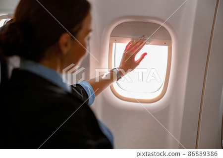 Female flight attendant closing window in aircraft 86889386