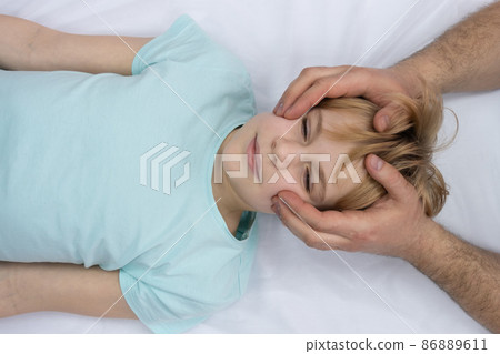 The osteopath works with the child's head. A teenage girl lies on a couch. The doctor gently palpates the head 86889611