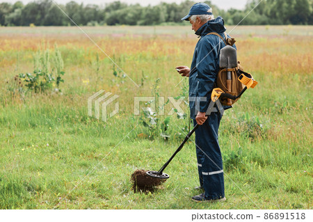 Profile portrait of treasure hunter in meadow, full length portrait of numismatist holding his finding coin under ground in field with metal detector. 86891518