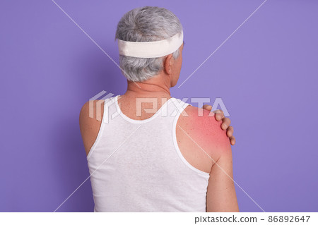 Back view of white haired senior man posing in studio against lilac wall, male being injured in gym, doing physical exercises, poses backwards, needed treatment, asks to call doctor. Health concept. 86892647