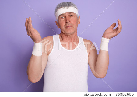 indoor shot of elderly man shrugging shoulders and spreading hands, showing helpless gesture, posing isolated over lilac studio background, senior male looks at camera with puzzled facial expression. indoor shot of elderly man shrugging shoulders and spreading hands, showing helpless gesture, posing isolated over lilac studio background, senior male looks at camera with puzzled facial expression. 86892690