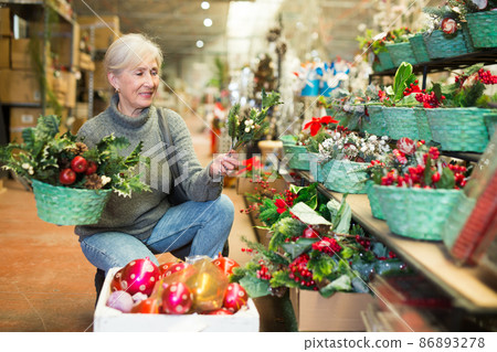 Smiling senior woman choosing Christmas decorations in store Smiling senior woman choosing Christmas decorations in store 86893278