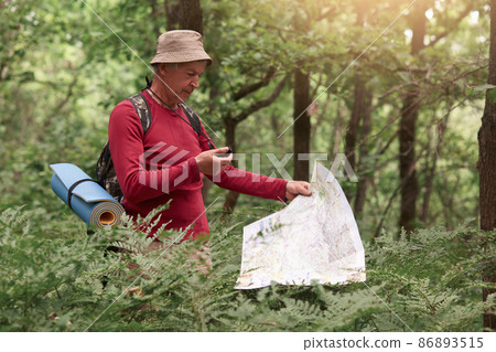 Coordination and navigation in the forest. Image of man holding compass and paper map in his hands, finding right way in wood, being lost while walking on path and enjoying beautiful nature. 86893515