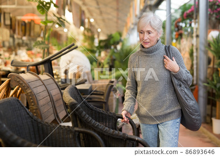 Elderly woman looking for plastic wicker chairs in furnishing store Elderly woman looking for plastic wicker chairs in furnishing store 86893646