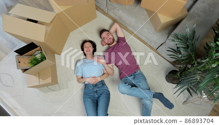 Happy couple lying on the floor in new home with cordboard boxes around. Couple moving to a new home. Relocating, new home and people concept. Top view. Happy couple lying on the floor in new home with cordboard boxes around. Couple moving to a new home. Relocating, new home and people concept. Top view. 86893704