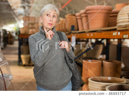 Senior woman looking for pots for growing plants in greenhouse Senior woman looking for pots for growing plants in greenhouse 86893717
