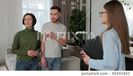 Close up of real estate agent woman shows modern house to a young couple. Young couple client rent investment. Close up of real estate agent woman shows modern house to a young couple. Young couple client rent investment. 86893803