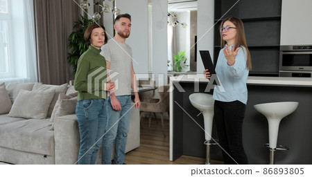 Real estate agent woman shows modern house to a young couple. Young couple client rent investment. 86893805
