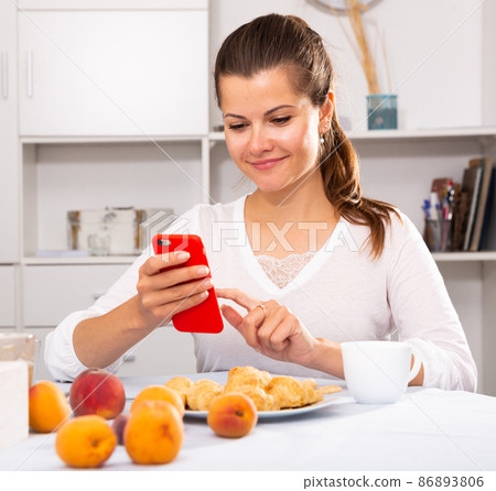 Smiling woman with phone during breakfast Smiling woman with phone during breakfast 86893806