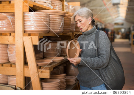 Elderly woman looking for flower pots in hypermarket Elderly woman looking for flower pots in hypermarket 86893894