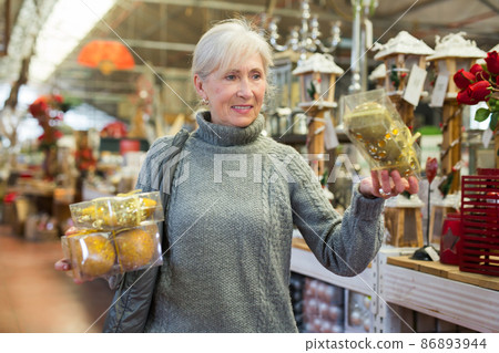 Elderly woman in festive mood choosing Christmas decorations in store 86893944