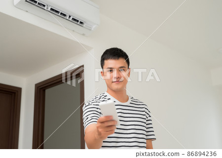 Air conditioner inside unit with man operating remote controller. / Air conditioner with remote controller 86894236