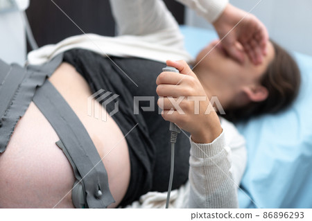 Tired Pregnant Woman On Hospital Couch During Medical Control Cardiotocography. Visit Gynecologist Doctor At Clinic For Pregnancy Consultant. Examine Expectant Belly Baby Mother Healthcare Check Up 86896293