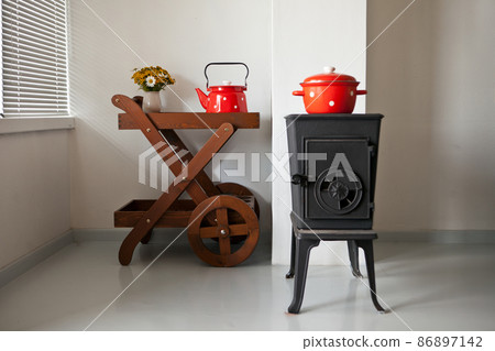 iron stove at home interior in country house. furnace is heated near window. red tableware on table iron stove at home interior in country house. furnace is heated near window. red tableware on table 86897142