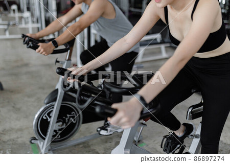 exercise concept The two sport club participants playing exercise bike machine for doing their cardio beside each other 86897274