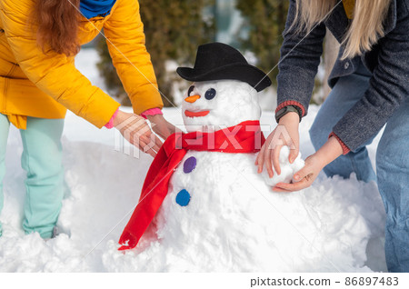 Two faceless Caucasian women are making a snowman. Winter fun. 86897483