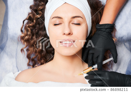 Cosmetologist's hands starting procedure of biorevitalization of decollete area for young curly woman. Anti aging skin rejuvenation procedure. Injections of beauty. Cosmetologist's hands starting procedure of biorevitalization of decollete area for young curly woman. Anti aging skin rejuvenation procedure. Injections of beauty. 86898211