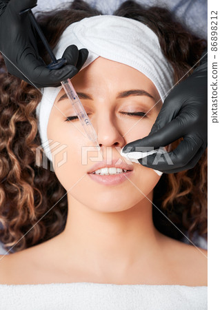 Close up portrait of beautician in black rubber gloves doing lip augmentation in professional beauty salon. Concept of process procedure for improvement lips with injection special preparation. Close up portrait of beautician in black rubber gloves doing lip augmentation in professional beauty salon. Concept of process procedure for improvement lips with injection special preparation. 86898212