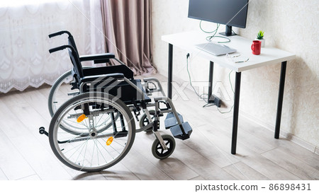 Workplace for a disabled person. Wheelchair at the table with a computer.  86898431