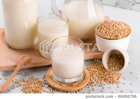Vegan non diary buckwheat milk in glasses with buckwheat groats in a bowl on white stone table, close up Vegan non diary buckwheat milk in glasses with buckwheat groats in a bowl on white stone table, close up 86898796