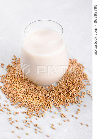 Vegan non diary buckwheat milk in glass with buckwheat groats on a white table. Veggies healthy milk product, close up Vegan non diary buckwheat milk in glass with buckwheat groats on a white table. Veggies healthy milk product, close up 86898799