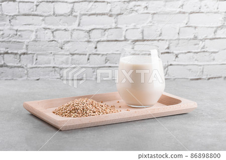 Vegan non diary buckwheat milk in glass on a wooden plate with buckwheat groats on a grey table. Veggies healthy milk 86898800