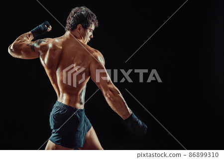 Side view of athlete shirtless boxer who strikes isolated on dark background. Sport concept Side view of athlete shirtless boxer who strikes isolated on dark background. Sport concept 86899310