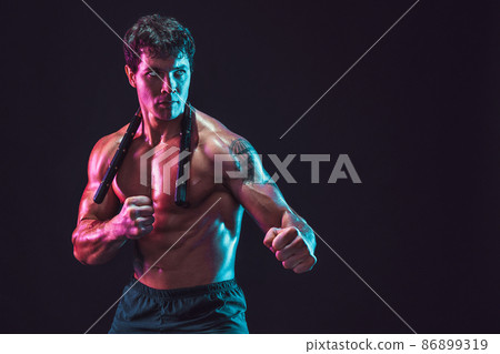 Half length of strong male athlete who poses with nunchaku on black background. Sport concept  86899319