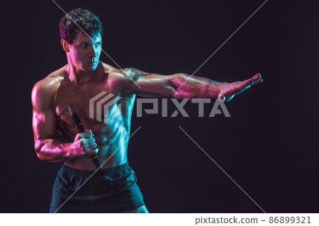 Portrait of muscular man who trains with nunchaku while isolated on black background. Sport concept 86899321