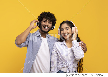 Happy indian couple in headphones listening to music and hugging over yellow studio background Happy indian couple in headphones listening to music and hugging over yellow studio background 86899570