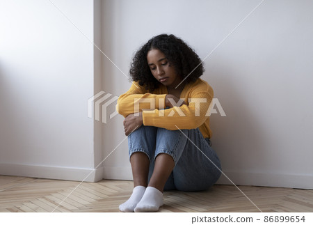 Full length of young black woman suffering from depression, sitting on floor and hugging her knees at home, copy space 86899654