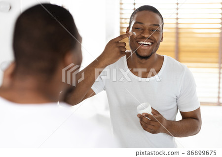 Skincare For Men. Happy Handsome Black Man Applying Moisturising Cream On Face 86899675