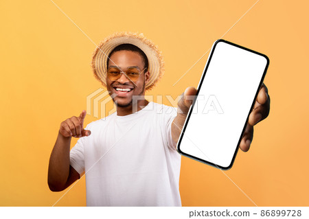 Excited black man in summer hat showing cellphone with blank screen, recommending mobile app for travelling Excited black man in summer hat showing cellphone with blank screen, recommending mobile app for travelling 86899728