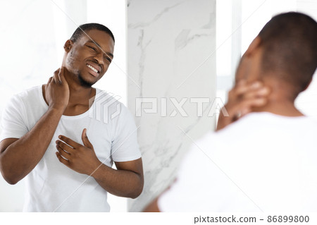 Unhappy Black Guy Suffering Neck Ache While Standing Near Mirror In Bathroom Unhappy Black Guy Suffering Neck Ache While Standing Near Mirror In Bathroom 86899800