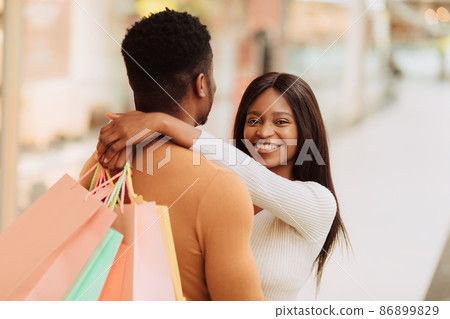 Cheerful young black couple hugging and holding shopping bags Cheerful young black couple hugging and holding shopping bags 86899829