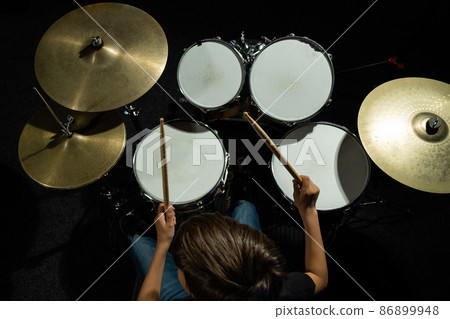 Top view of a boy learning to play the drums in the studio on a black background. A student of a music school. Top view of a boy learning to play the drums in the studio on a black background. A student of a music school. 86899948