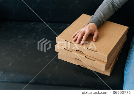Close-up high-angle view of unrecognizable courier male holding boxes pizza waiting customer, sitting on sofa with in hall of office or apartment building, cropped shot. Close-up high-angle view of unrecognizable courier male holding boxes pizza waiting customer, sitting on sofa with in hall of office or apartment building, cropped shot. 86900775