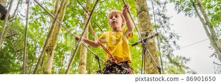 Little boy in a rope park. Active physical recreation of the child in the fresh air in the park. Training for children BANNER, LONG FORMAT 86901650