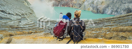 BANNER, LONG FORMAT Young tourist man and woman sit at the edge of the crater of the Ijen volcano or Kawah Ijen on the Indonesian language. Famous volcano containing the biggest in the world acid lake 86901780