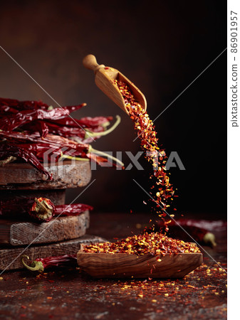 Chilli flakes are poured into a wooden dish. 86901957
