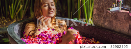 Attractive Young woman in bath with petals of tropical flowers and aroma oils. Spa treatments for skin rejuvenation. Alluring woman in Spa salon. Girl relaxing in bathtub with flower petals. Luxury Attractive Young woman in bath with petals of tropical flowers and aroma oils. Spa treatments for skin rejuvenation. Alluring woman in Spa salon. Girl relaxing in bathtub with flower petals. Luxury 86902595
