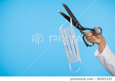 Tailor's scissors cut through the face mask, heralding the end of the global COVID-19 pandemic. 86905281