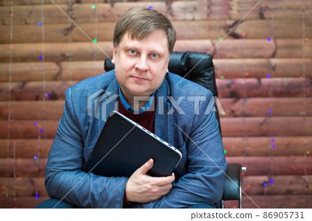 An adult with a blond man with a laptop on a leather chair in the office on a wooden background with garlands 86905731
