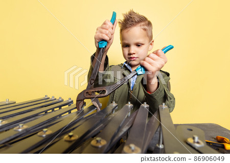 Cute little boy, child in image of auto mechanic or fitter in dungarees with work tools repairing auto motor isolated on yellow background. 86906049